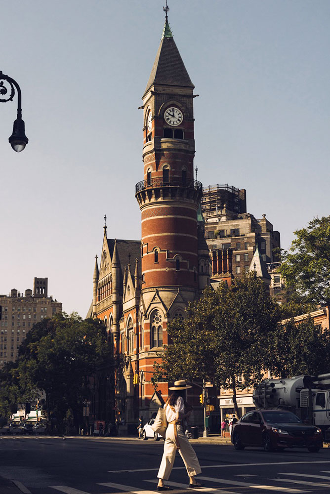 Street view of the Jefferson Market Library in Manhattan with a brick clock tower rising from the corner of the building.